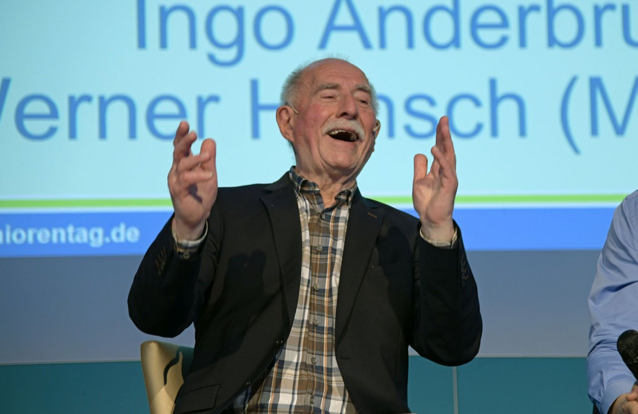 Werner Hansch sitting on the stage laughing
