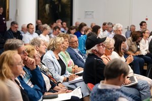Ein Publikum aus älteren Menschen sieht gespannt richtung Rednerpult.