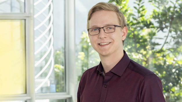 Portrait Tobias Lipka: Junger Mann mit brille und kurzem blonden Haar. Er trägt ein dunkelrotes Hemd.