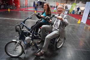 Franz Müntefering und eine Frau fahren auf einem Fahrrad mit drei Rädern und zwei Sitzen