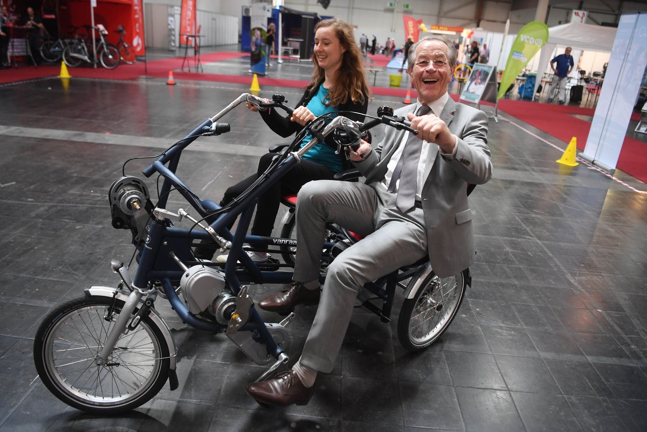 Franz Müntefering und eine Frau fahren auf einem Fahrrad mit drei Rädern und zwei Sitzen