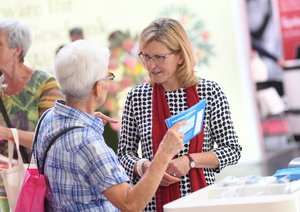Eine ältere Frau unterhält sich mit einer anderen Frau mittleren Alters am Stand. Sie hat eine Broschüre in der Hand.
