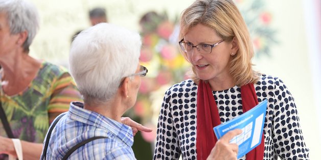 Eine ältere Frau unterhält sich mit einer anderen Frau mittleren Alters am Stand. Sie hat eine Broschüre in der Hand.