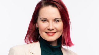 Portrait Straub: Eine junge Frau mit rötlichem schulterlangem Haar. Sie trägt einen schwarzen Rollkragenpullover und einen hellen Blazer.