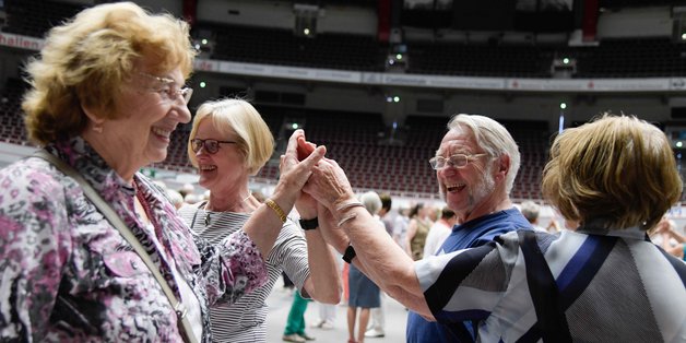 Drei Frauen und ein Mann tanzen im Kreis und halten sich in der Mitte an den Händen.