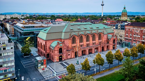 Congress-Center Rosengarten in Mannheim: Ein roter alter Backsteinbau mit grünem Dach. Er ist eingebettet in mehreren Gebäuden. Rund um das Gebäude sind Straßen. 