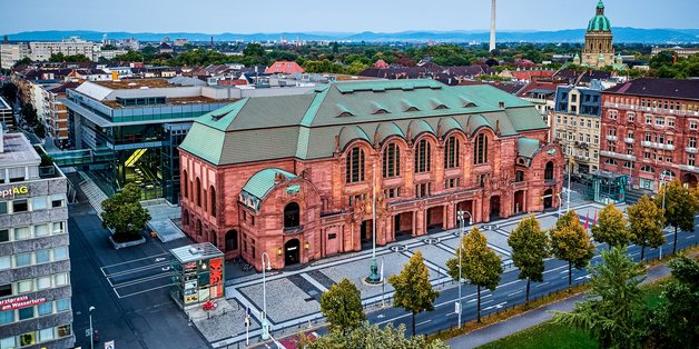 Congress-Center Rosengarten in Mannheim: Ein roter alter Backsteinbau mit grünem Dach. Er ist eingebettet in mehreren Gebäuden. Rund um das Gebäude sind Straßen. 