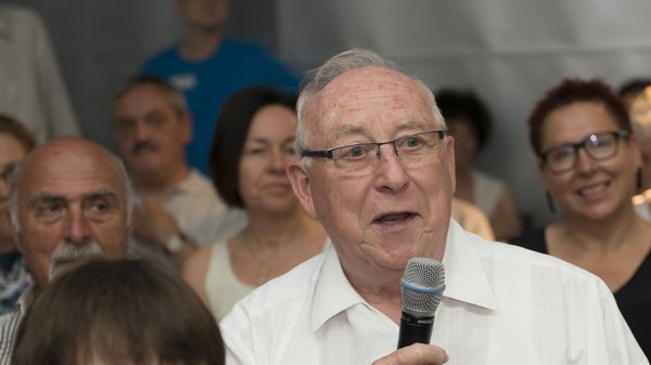 Älterer Mann sitzt unter den Zuschauern. Er spricht in ein Mikrofon