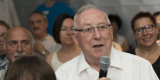 Älterer Mann sitzt unter den Zuschauern. Er spricht in ein Mikrofon