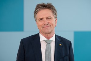 Porträtfoto des Ministers für Soziales, Gesundheit und Integration des Landes Baden-Württemberg Manne Lucha MdL: Ein älterer Mann mit dunkelgrauen Haaren trägt einen Anzug mit Krawatte.