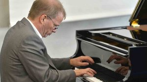 Prof. Dr. Andreas Kruse, ein älterer Mann mit Brille und Anzug, spielt am Flügel.