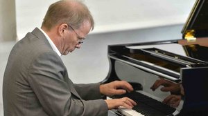 Prof. Dr. Andreas Kruse, ein älterer Mann mit Brille und Anzug, spielt am Flügel.