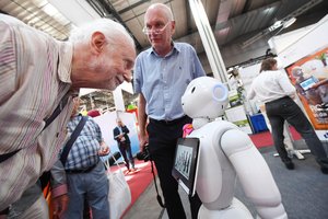 Ein alter Mann bückt sich vor einem Roboter. Er schaut ihm ins Gesicht.