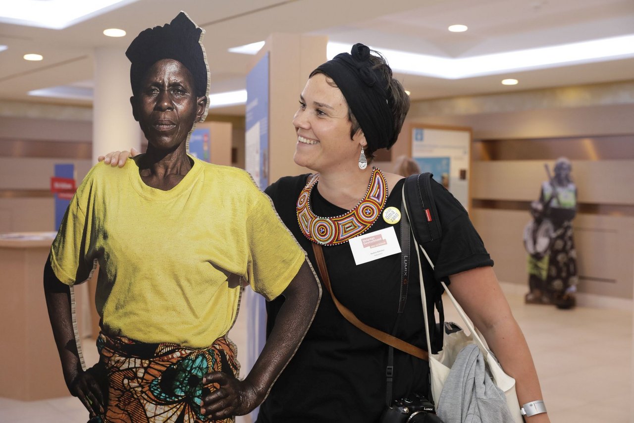 Eine Frau lächelt einen lebensgroßen Pappaufsteller einer afrikanischen Frau an.