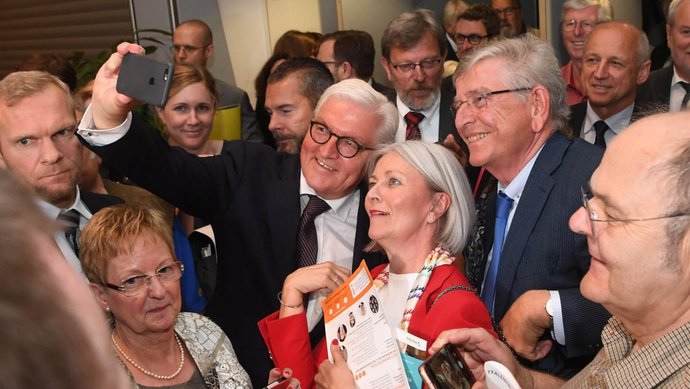 Der Bundespräsident Frank-Walter Steinmeier macht ein Selfie mit einer Frau in der Menge.