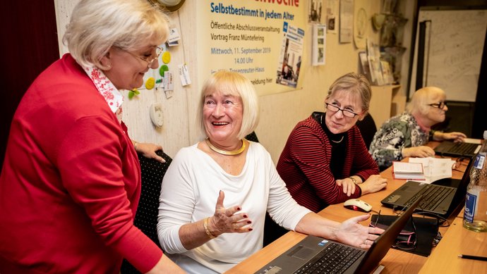 Drei ältere Frauen sitzen vor ihren Laptops und vierte gibt Tipps.