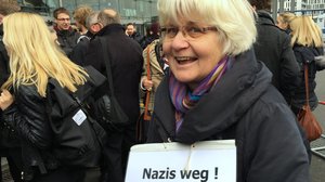 ©Irmela Mensah-Schramm Eine Frau mit weißen kinnlangen Haaren und Brille trägt ein Schild auf dem „Nazis weg!“ steht.