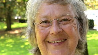 Eine ältere Frau mit grauen Haaren und rahmenloser Brille.